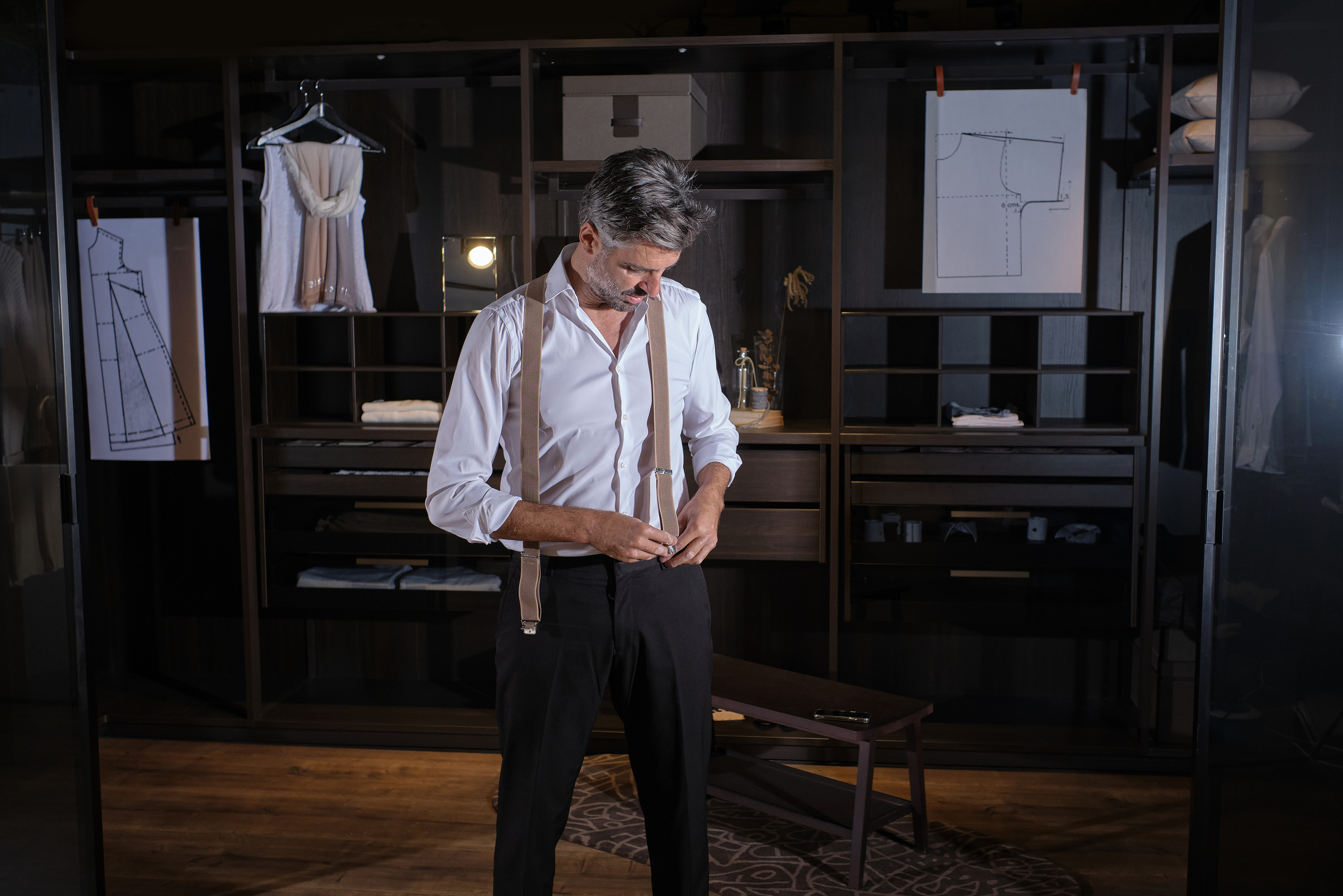 Confident gray haired man putting on suspenders for trousers in dressing room